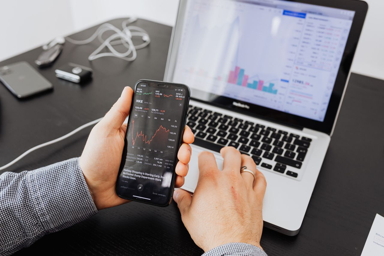 gallery-1 Person analyzes stock data with a smartphone and laptop, indoors.